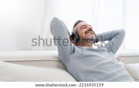 Portrait of senior old caucasian man stay home sit on the sofa living room listen to music head phone. Happy moment of pure love middle age male relax with gadget online digital technology in winter Royalty-Free Stock Photo #2216935159