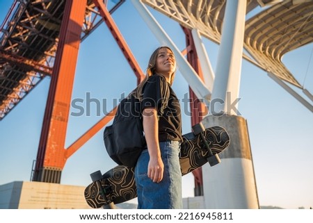 Blonde teen girl looking at the distance while standing with her skateboard at the port