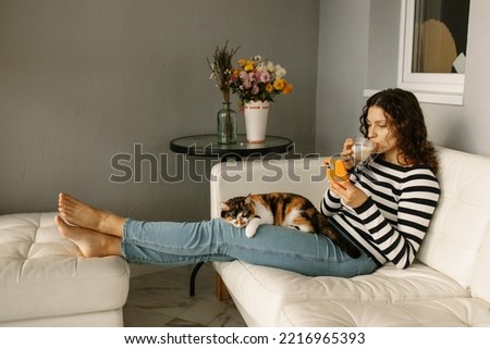 Young woman is using her  smartphone at home with a cat on her lap