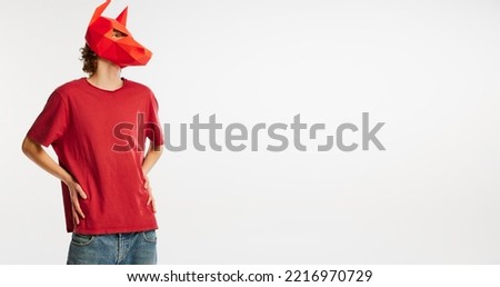 Young man in red t-shirt with cardboard animal mask on his head isolated on white background. Concept of art, fashion, creativity, funny meme emotions. Copy space for ad