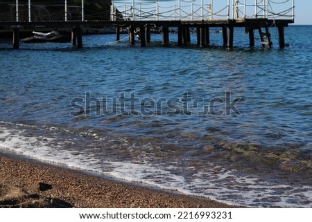 photo of the wavy foamy sea, the wooden scaffold on the seashore, the last light of the sun reflecting on the coastline