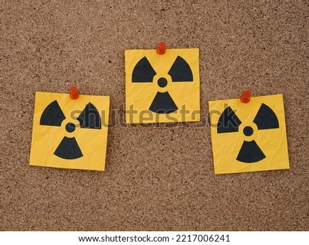 Three yellow paper notes with radiation warning signs on them pinned to a corkboard. Close up. Royalty-Free Stock Photo #2217006241