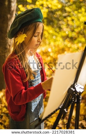 A girl with paints and an easel paints a landscape of an autumn forest. Autumn forest landscape. A girl artist paints an autumn forest. A creative child.