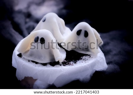 Homemade Halloween sweet covered with white fondant in a shape of a ghost. Two other similarly shaped sweets blurry visible in the background.   Royalty-Free Stock Photo #2217041403