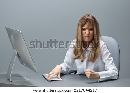 Irritated pretty blonde businesswoman worker freelancer show fist using desktop computer sitting at workplace in gray modern office. Remote Job, Technology And Career Profession Concept. Copy space