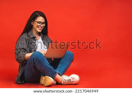 Business concept. Portrait of smiling happy brunette woman in casual sitting on floor in lotus pose and holding laptop isolated over red background. 