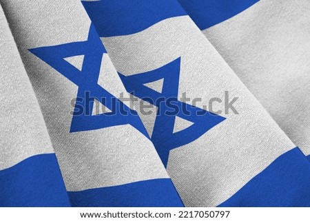 Israel flag with big folds waving close up under the studio light indoors. The official symbols and colors in fabric banner