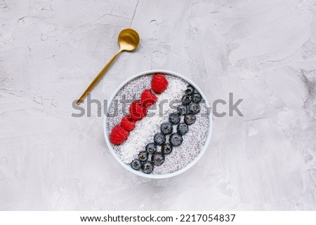 Overnight chia seed pudding with fresh blueberries, raspberries and coconut flakes in a bowl with golden spoon Copy space, top view. Breakfast, superfood and vegan food concept. Gray background Royalty-Free Stock Photo #2217054837