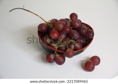 Red grapes in a black bowl on a white background.