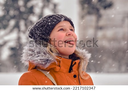 A 10-12 years old girl catches snowflakes with her tongue. The child plays with snow. The first snow fell.