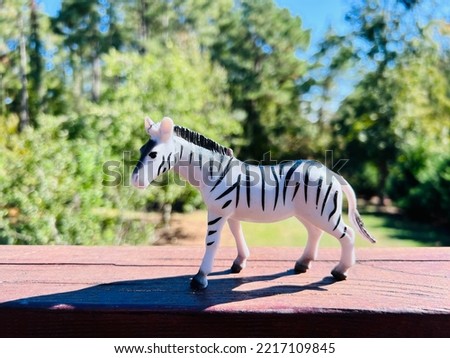 Small toy zebra in the sunlight on a red wooden deck