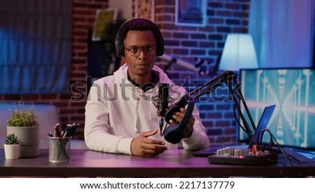 African american content creator recording product review testing headphones using professional audio equipment in home studio. Male influencer brodcasting presentation for wireless headset.