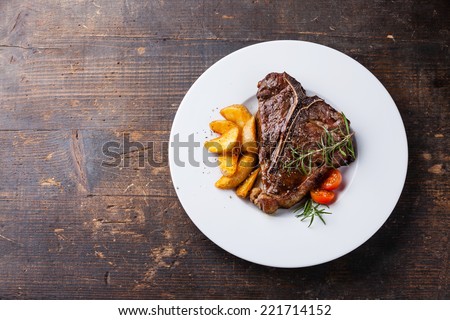 T-Bone Steak with roasted potato wedges on white plate on wooden background Royalty-Free Stock Photo #221714152