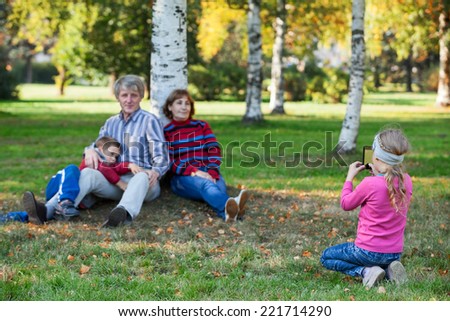 Young pretty girl photographing her family by phone in autumn park