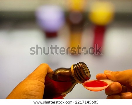 Hand pours cough syrup, fever medicine and cold containing paracetamol into measuring spoon