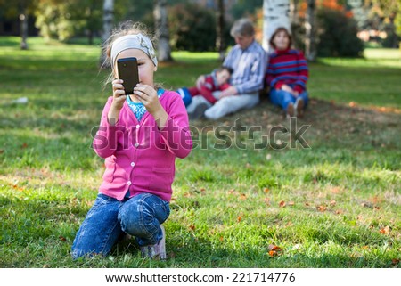 Pretty Caucasian girl making picture with phone, father, mother and brother are on background