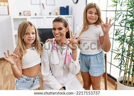 Pediatrician woman working at the clinic with two little girls doing ok sign with fingers, smiling friendly gesturing excellent symbol 