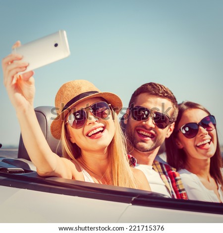 Capturing a moment. Three young happy people enjoying road trip in their white convertible and making selfie