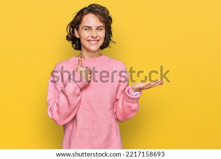 Young hispanic woman wearing casual clothes showing palm hand and doing ok gesture with thumbs up, smiling happy and cheerful 