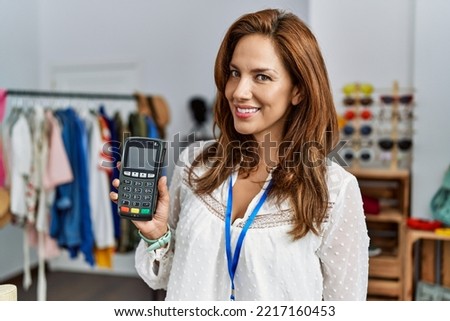 Young latin woman shopkeeper using data phone working at clothing store
