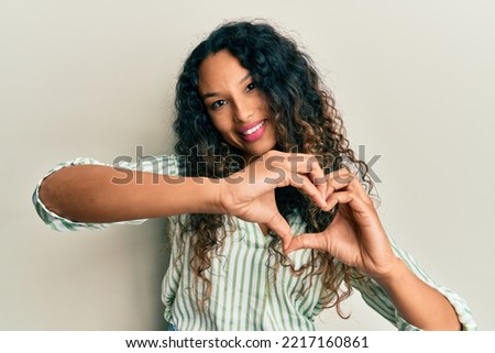 Young latin woman wearing casual clothes smiling in love doing heart symbol shape with hands. romantic concept. 