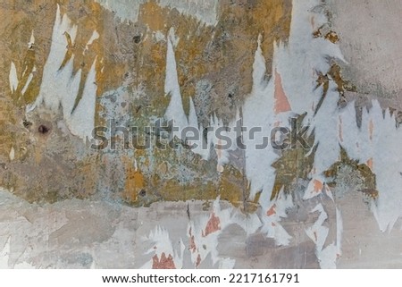Old dilapidated wall with pieces of paper wallpaper and layers of multi-colored plaster. Architectural vintage texture with scratches and abrasions on the surface