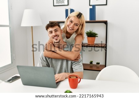 Young caucasian couple hugging and using laptop sitting on the desk at home.