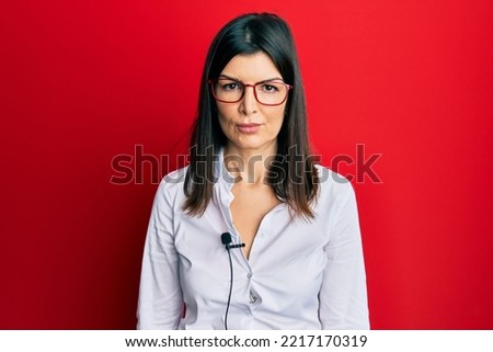 Young hispanic woman using lavalier microphone thinking attitude and sober expression looking self confident 