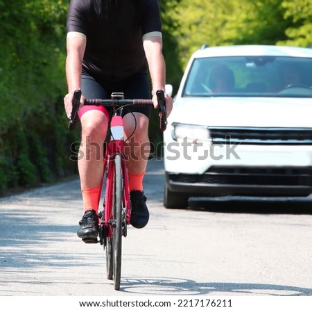 cyclist with the bike rides on the road and he risks an accident with the car behind