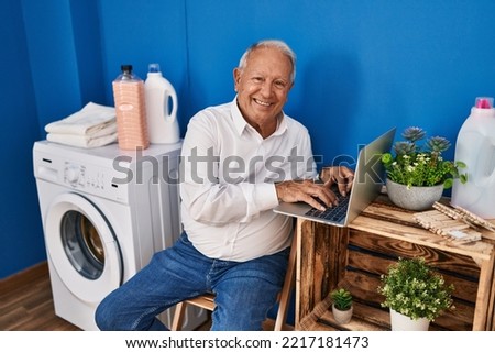 Senior man using laptop waiting for washing machine at laundry room