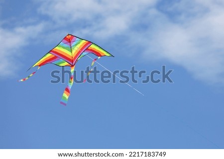 colorful kite with the multi colors of the rainbow flies free in the sky and some white clouds