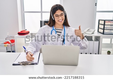 Young brunette woman working on online appointment smiling happy and positive, thumb up doing excellent and approval sign 
