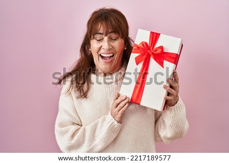 Middle age hispanic woman holding present smiling and laughing hard out loud because funny crazy joke. 
