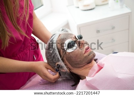 Portrait of an adult woman lying with her eyes closed during the carbon peeling procedure.