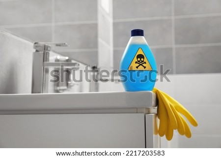 Bottle of toxic household chemical with warning sign and gloves in bathroom, space for text Royalty-Free Stock Photo #2217203583