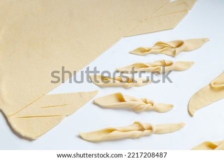 Raw dough on a light table. Cooking traditional cookies - Brushwood or chiacchiere. Royalty-Free Stock Photo #2217208487