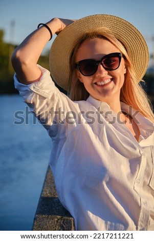 young happy blond woman in straw hat and sunglasses at summer sunset park looking at camera and smiling