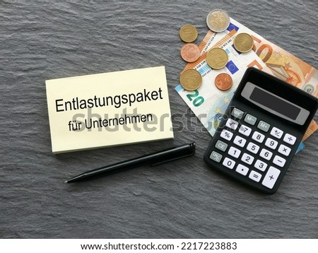 Calculator, money and a notepad with the German text Entlastungspaket für Unternehmen. Translated means relief package for compan Royalty-Free Stock Photo #2217223883