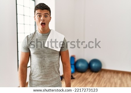 Young hispanic man wearing sportswear and towel at the gym afraid and shocked with surprise expression, fear and excited face.  Royalty-Free Stock Photo #2217273123