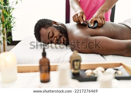 African american man reciving back massage with black stones at beauty center. Royalty-Free Stock Photo #2217276469