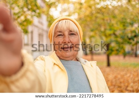 Beautiful happy 50s woman walking outdoors in autumn spring park take a selfie by camera.