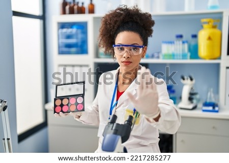 Young african american woman working at scientist laboratory doing make up with open hand doing stop sign with serious and confident expression, defense gesture 