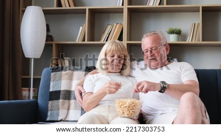Happy elderly married couple watching tv sitting on sofa, old couple eating popcorn and laughing