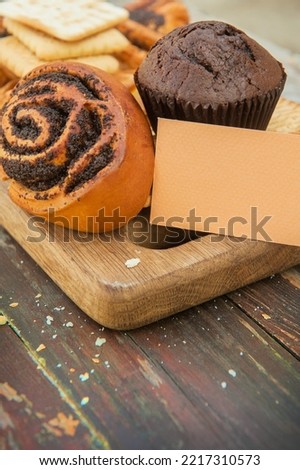 Cinnamon bun and chocolate muffin on a vintage style wooden backdrop with empty business card template