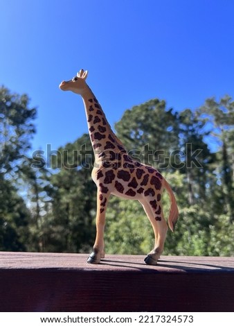 Toy giraffe enjoying the sunshine on a warm autumn day. Blue sky and trees in the background.