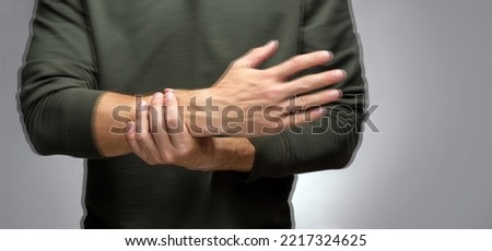 a man with a tremor tries to keep his hand from trembling with the help of the other. Royalty-Free Stock Photo #2217324625