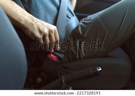 A man is driving down the road in his car and fastening his seat belt, close-up view of the hand and clasp inside the automobile, safe driving according to the rules of the road. Royalty-Free Stock Photo #2217328191