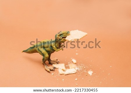 Tyrannosaurus rex with a biscuit in its mouth. Crumbled biscuit around him on brown background.