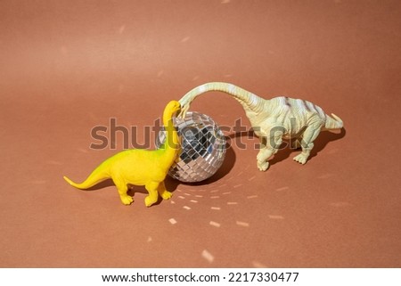 Two dinosaurs with disco ball on a brown background. Plastic toys. Minimal design.