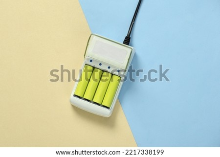 Battery charger with AA rechargeable batteries on blue yellow pastel background Royalty-Free Stock Photo #2217338199